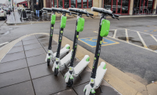 A row of four stationary Lime e-scooters on a wet sidewalk