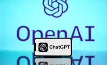 The ChatGPT logo is seen displayed on a mobile phone screen with OpenAI logo in the background.