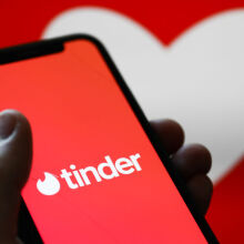 Tinder logo displayed on a phone screen and a heart shape displayed on a screen in the background.