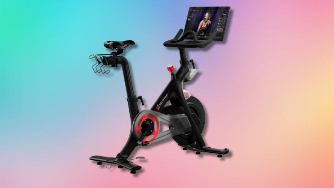 A black Peloton stationary bike with a red wheel and a large touchscreen displaying a fitness instructor.