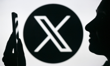 X logo behind user on smartphone