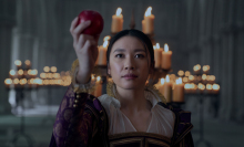 A woman in a 17th century England dress holds out an apple.