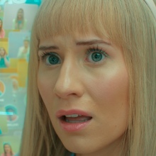 A blonde woman surrounded by virtual images of friends and the Doctor (Ncuti Gatwa).