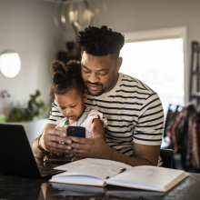 father and daughter sitting at the kitchen counter on laptop and phone