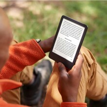 a person reads on a kindle e-reader while sitting on the ground outside