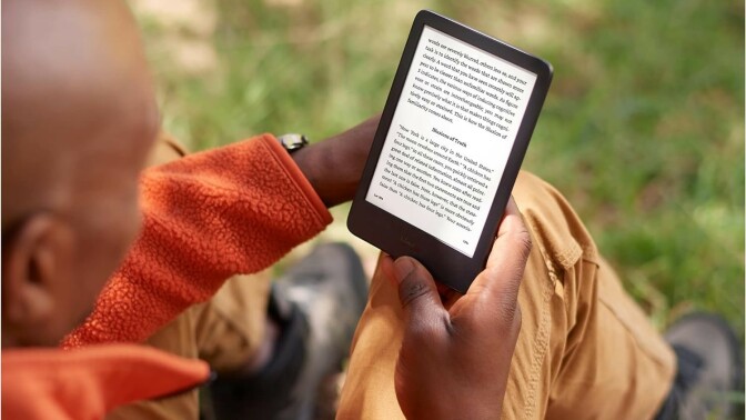 a person reads on a kindle e-reader while sitting on the ground outside