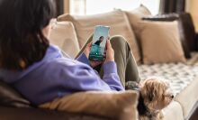 a person sits on a couch while looking at the calm app on a smartphone. A small dog is also lounging on the couch