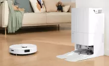White Roborock robot vacuum cleaning hardwood floor with dock and living room scene in peripherals