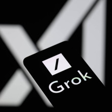 The Grok logo is being displayed on a smartphone with the X AI icon visible in the background.