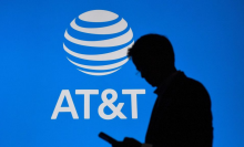 The silouhette of a man looking down as his smartphone as he walks past the AT&T logo.