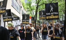 A group of striking people in black shirts holding signs that say "SAG-AFTRA on strike!" walk the streets of New York.