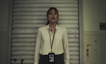 A woman in a blood-spattered white button-up shirt presses her back up against the wall of an interrogation room.