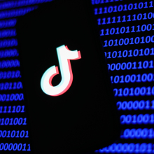 A phone showing the TikTok label in front of lines of binary code.