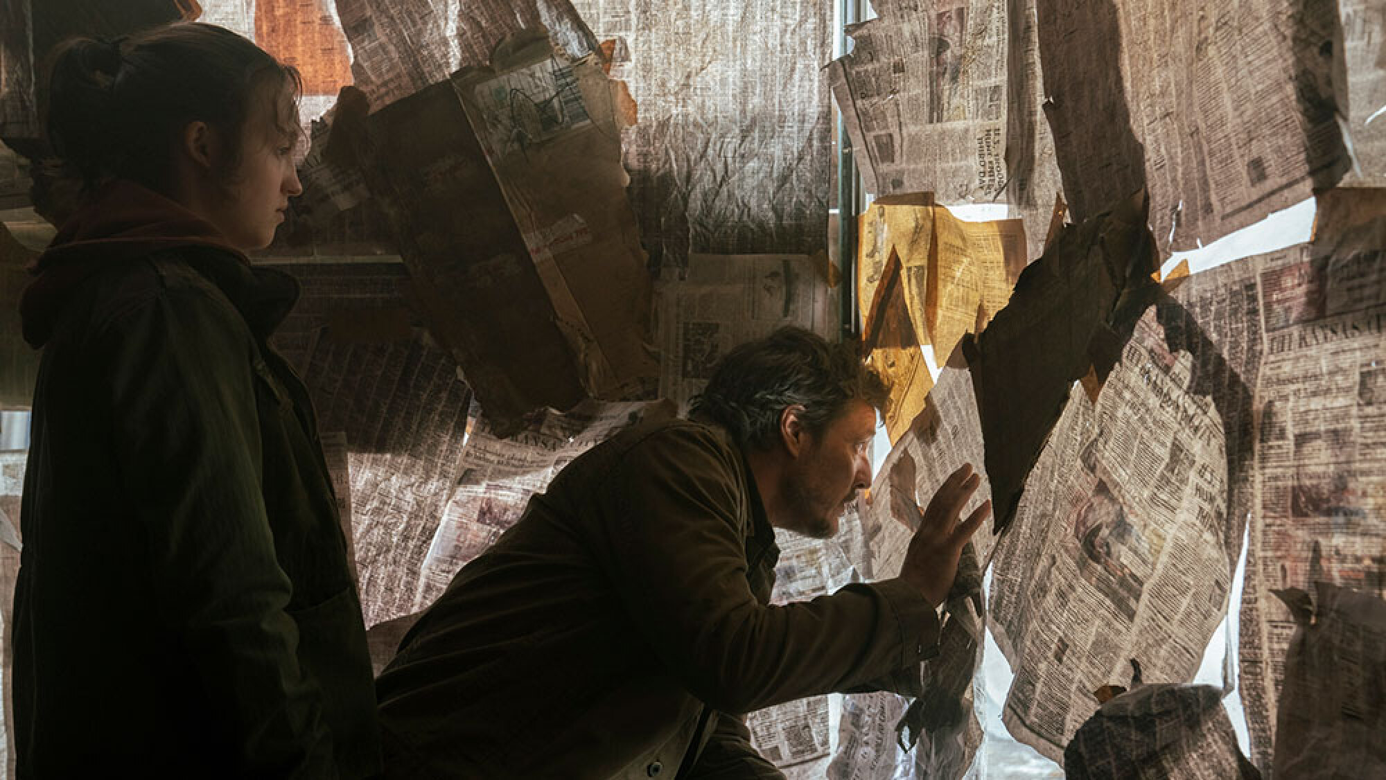 A man peers through a window covered in newspapers while a young girl looks on.