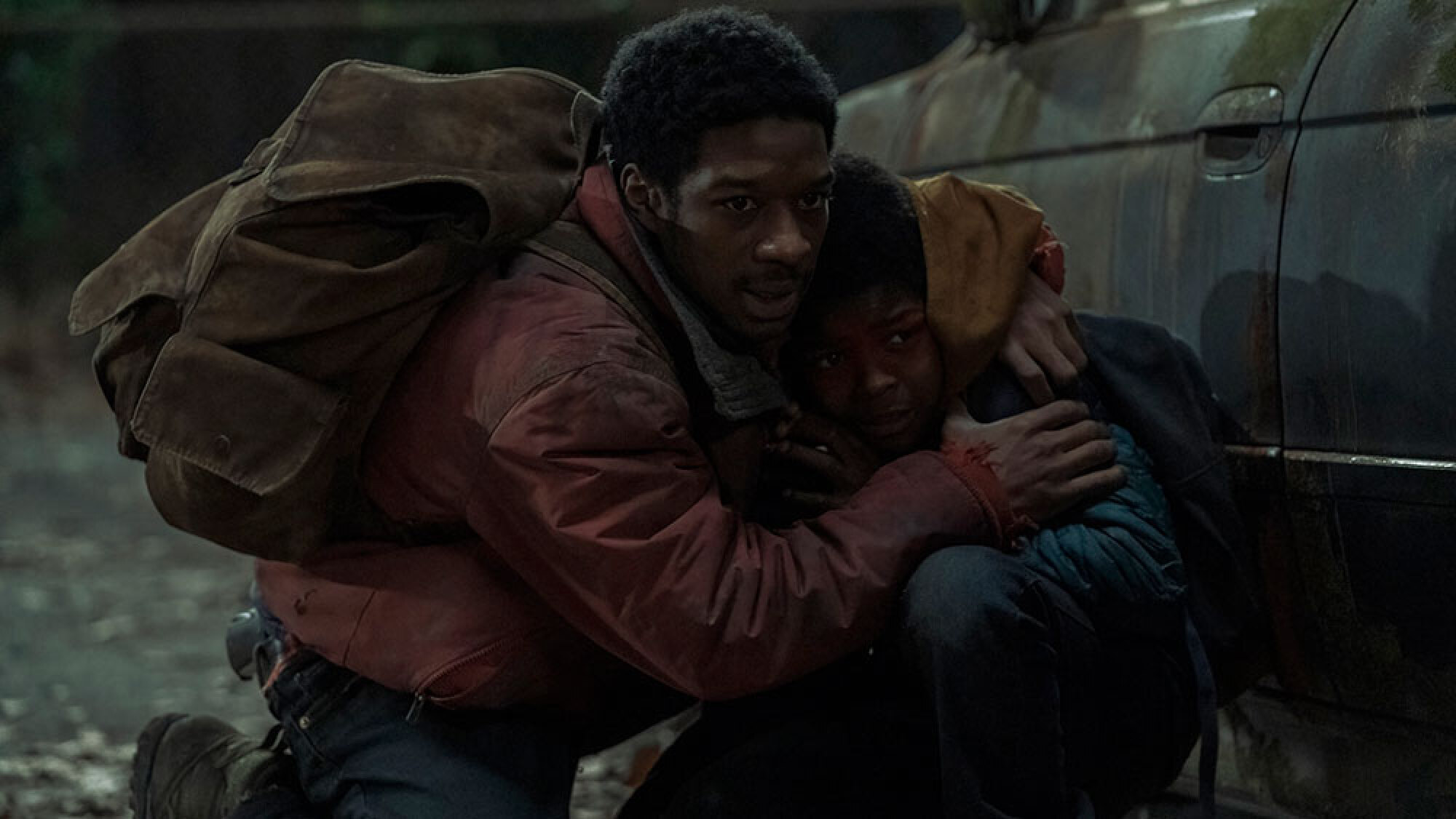 A man crouches by a car with his arms wrapped around a young boy.