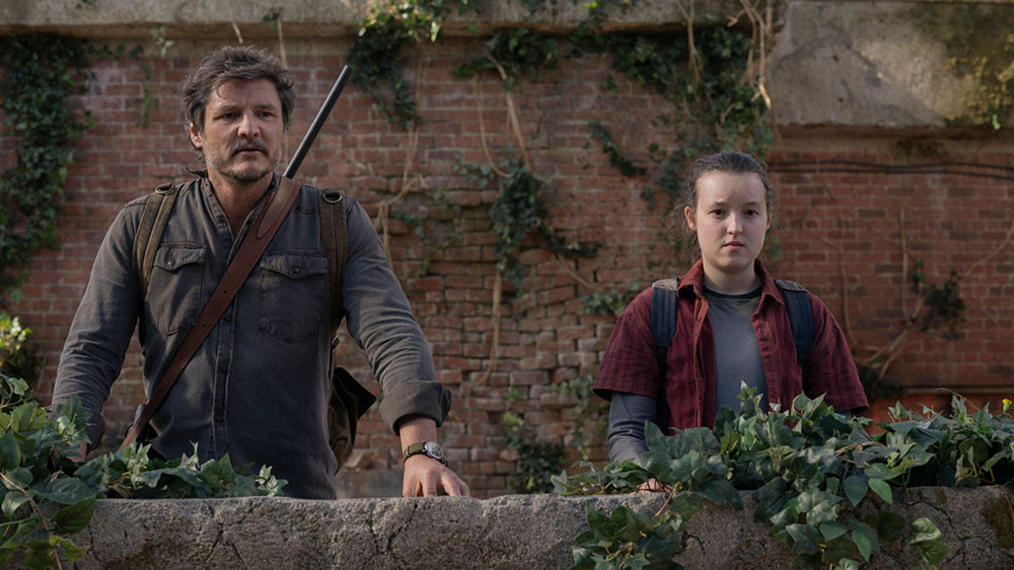 A man with a rifle slung over his back stands next to a young girl, both of them staring in the direction of the camera at something.