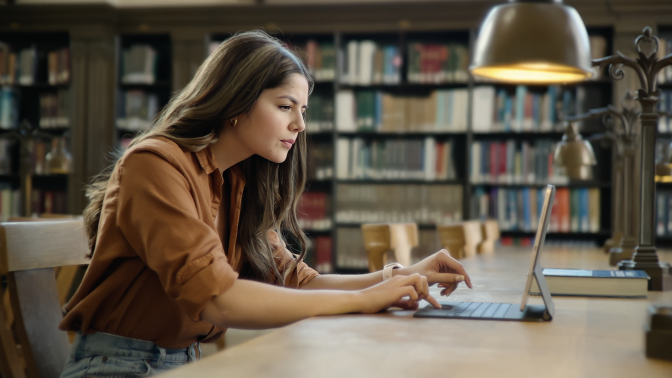 Person typing on Magic Keyboard attached to iPad Pro with library scene in background