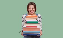 A person holding a stack of books against a green background.