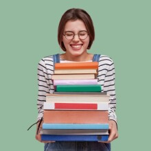 A person holding a stack of books against a green background.