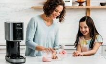 a mom makes ice cream with the ninja creami machine while daughter looks on smiling