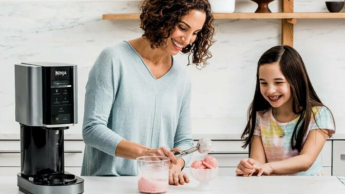 a mom makes ice cream with the ninja creami machine while daughter looks on smiling