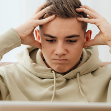 Person holding their head in frustration while looking at computer