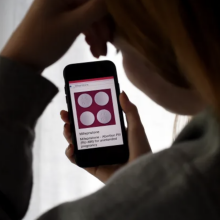 A woman holds a phone showing abortion pills on the screen.