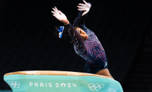 A gymnast twists their body in the air as the float over a green vault apparatus. 