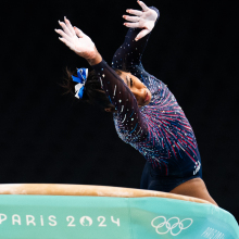 A gymnast twists their body in the air as the float over a green vault apparatus. 