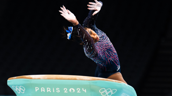 A gymnast twists their body in the air as the float over a green vault apparatus. 