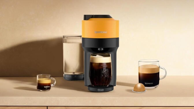 a mango-colored nespresso machine sits on a kitchen counter with several cups of coffee around it