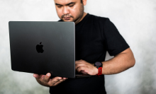 An out of focus man holding an in focus Macbook.