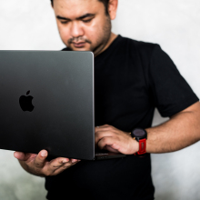 An out of focus man holding an in focus Macbook.