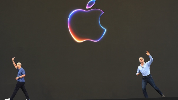 Tim Cook leaves a stage with a large Apple logo as Craig Federighi arrives from the other side