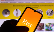 The Etsy logo on a smart phone in front of a desktop screen displaying an Etsy feed.