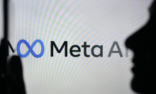 A person holding a cell phone in front of the Meta AI logo displayed on a computer screen, on April 29, 2024, in Edmonton, Canada.