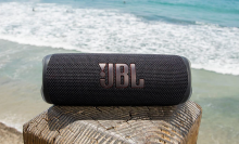 black JBL portable speaker on a wood block against a beach 