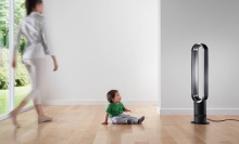 a woman walks across the room to her child who's sitting on the floor in front of a dyson fan