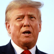 A man in a suit and red tie speaks.