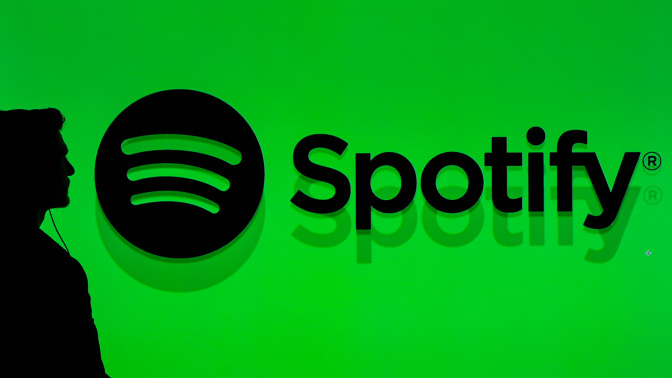 The silhouette of a man in front of a bright green backdrop that reads, "Spotify" with the Spotify logo next to it. 