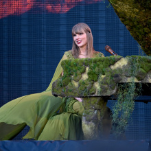 Taylor Swift sitting at a piano in a green dress. 
