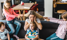 Small kids spending time with their frustrated nanny at home. Little girls are having fun while pulling her hair.