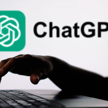 hand typing on a laptop in front of the ChatGPT logo on a wall