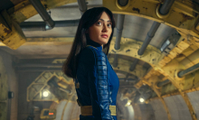 Ella Purnell (Lucy) stands in a vault corridor wearing a blue and yellow jumpsuit in "Fallout".