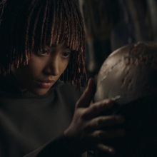 Osha holds the Stranger's cortosis helmet close to her face, examining it.