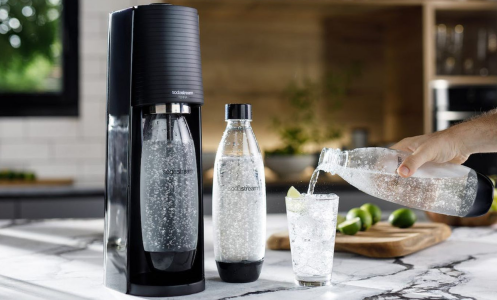 Person pouring sparkling water into glass next to SodaStream sparkling water maker on countertop