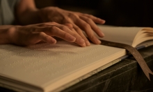 A pair of hands glide over lines of braille in a book. 