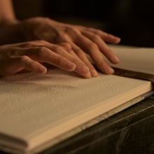 A pair of hands glide over lines of braille in a book. 