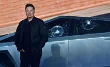 Elon Musk standing in front of a Cybertruck with two bullet marks in its windows.