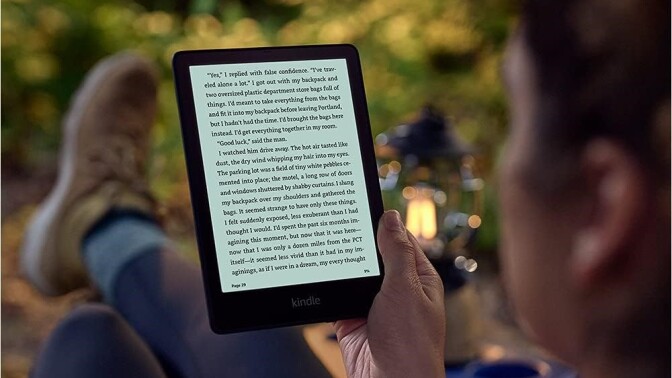 a person reads a book on an amazon kindle ereader while sitting in the woods